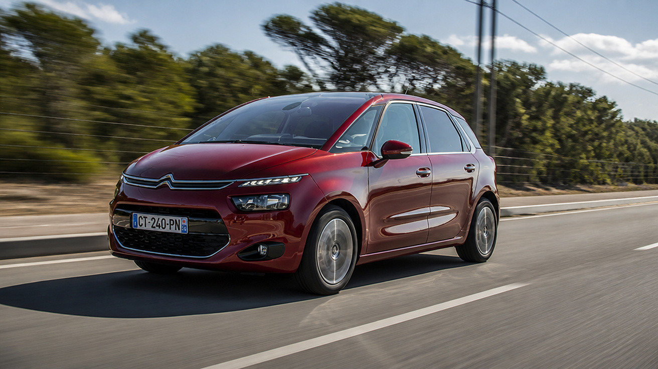 Red Citroën C4 Picasso driving on a road with trees and clear sky in the background.
