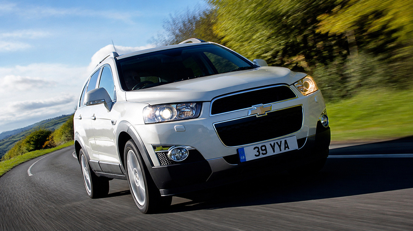 White Chevrolet SUV driving on a winding road with greenery and blue sky in the background.