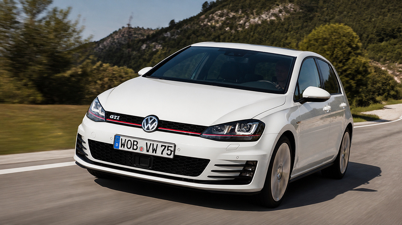 White Volkswagen Golf GTI driving on a curved road with trees and hills in the background.