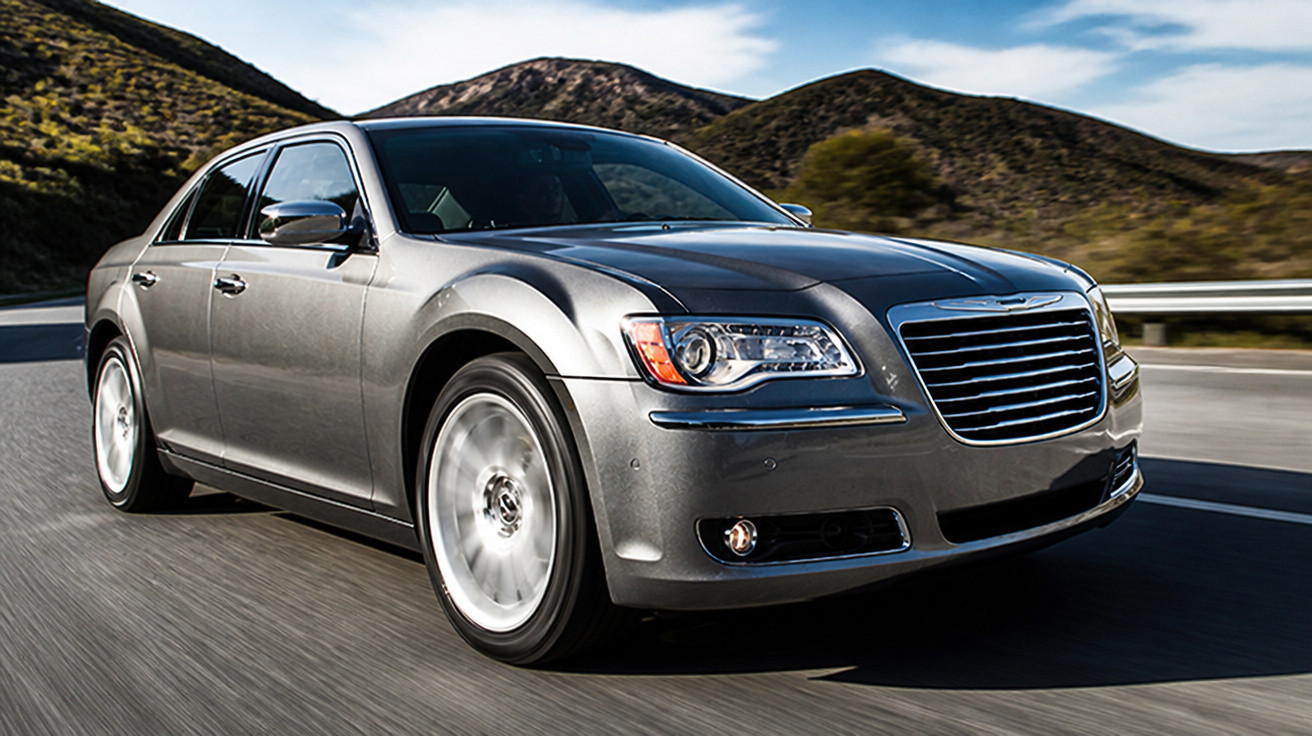 Silver luxury sedan driving on a highway with hills and blue sky in the background.