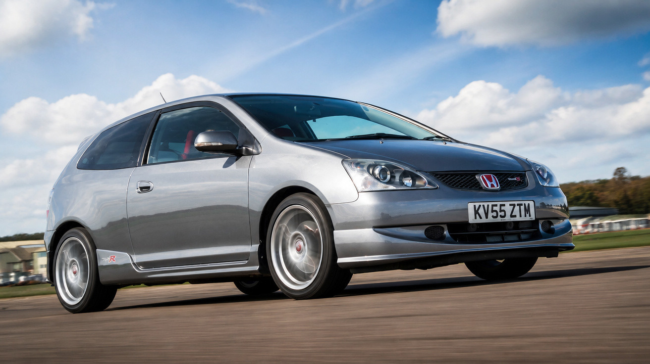 Silver Honda Civic Type R speeding on a racetrack under a partly cloudy blue sky.