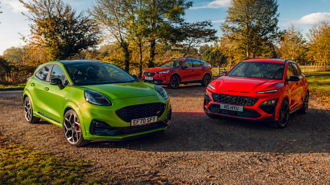 Three sporty compact SUVs in green and red colours parked on a gravel path with autumn trees in the background.