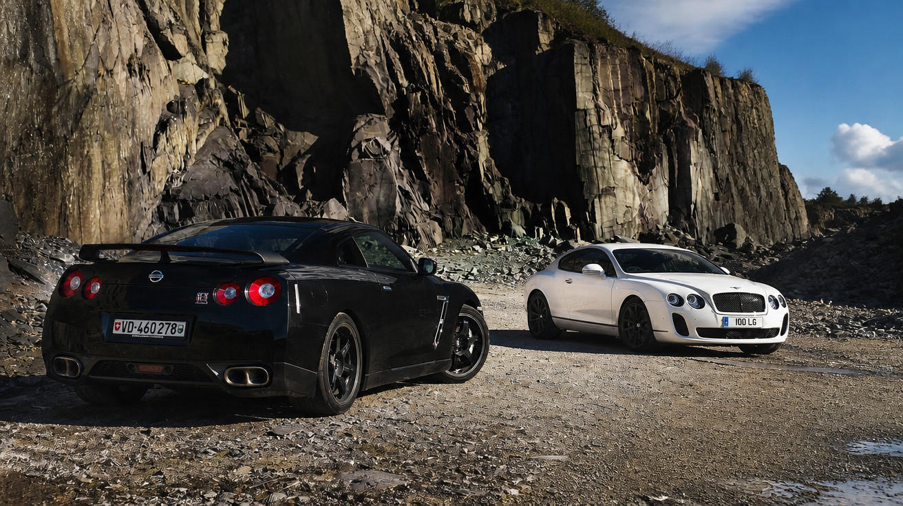 Two sports cars, a black Nissan GT-R and a white Bentley Continental GT, parked on rocky terrain by cliffs.