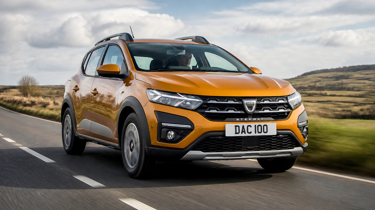 Orange Dacia Stepway SUV driving on a countryside road with clear skies and rolling hills in the background.