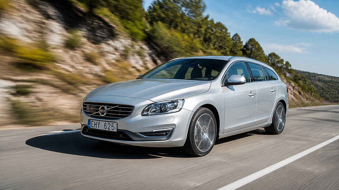 Silver Volvo station wagon driving on a winding road with rocky hillside and trees in the background.