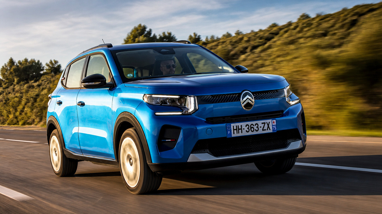 Blue Citroën SUV driving on a road with green trees and cloudy sky in the background.