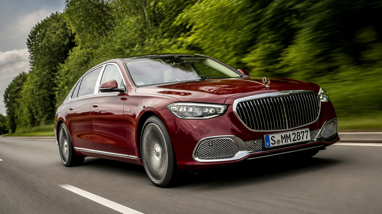 Maroon Mercedes-Benz luxury sedan driving on a road with green trees in the background.