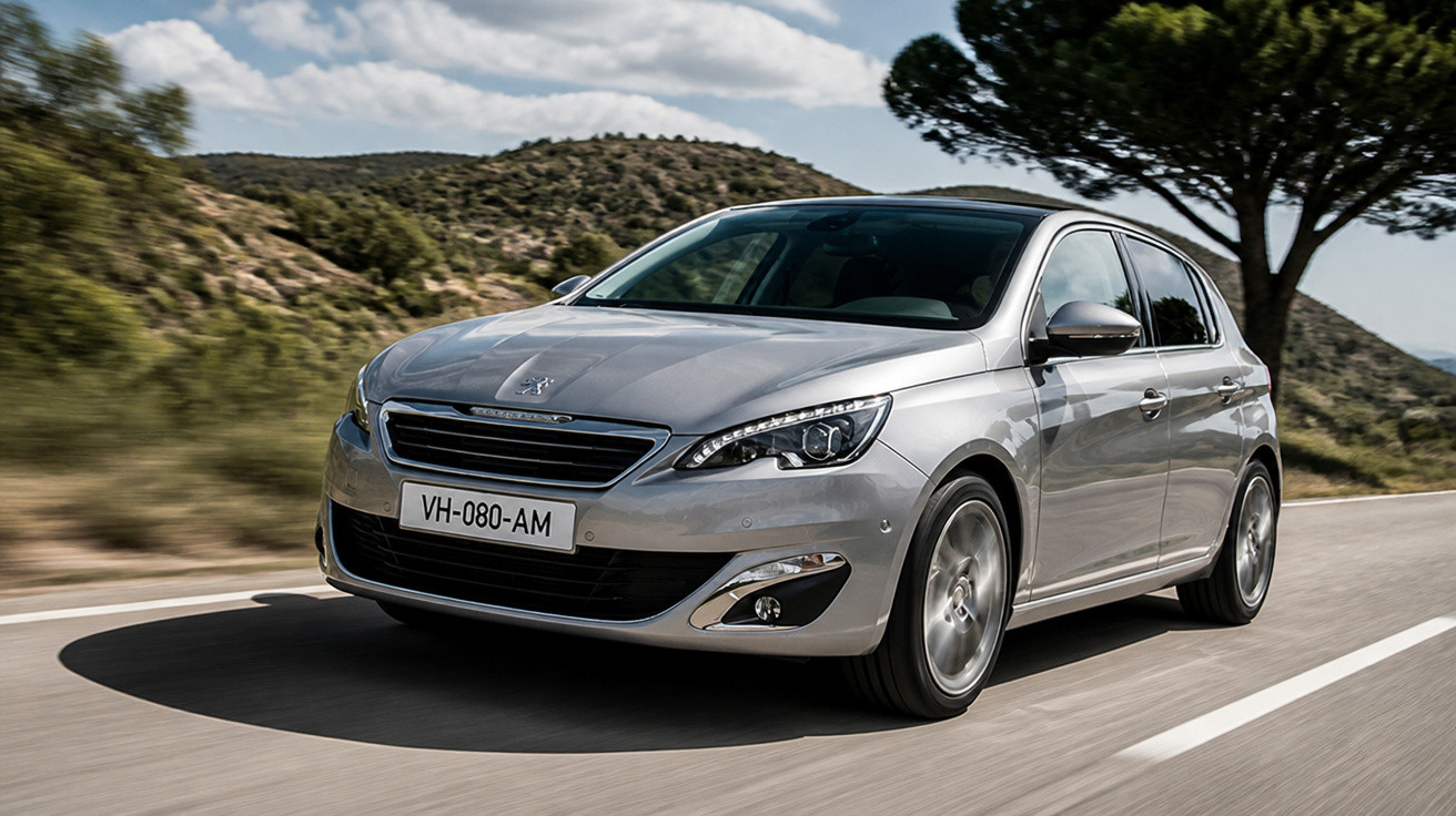 Silver Peugeot hatchback driving on a mountain road under a partly cloudy sky.