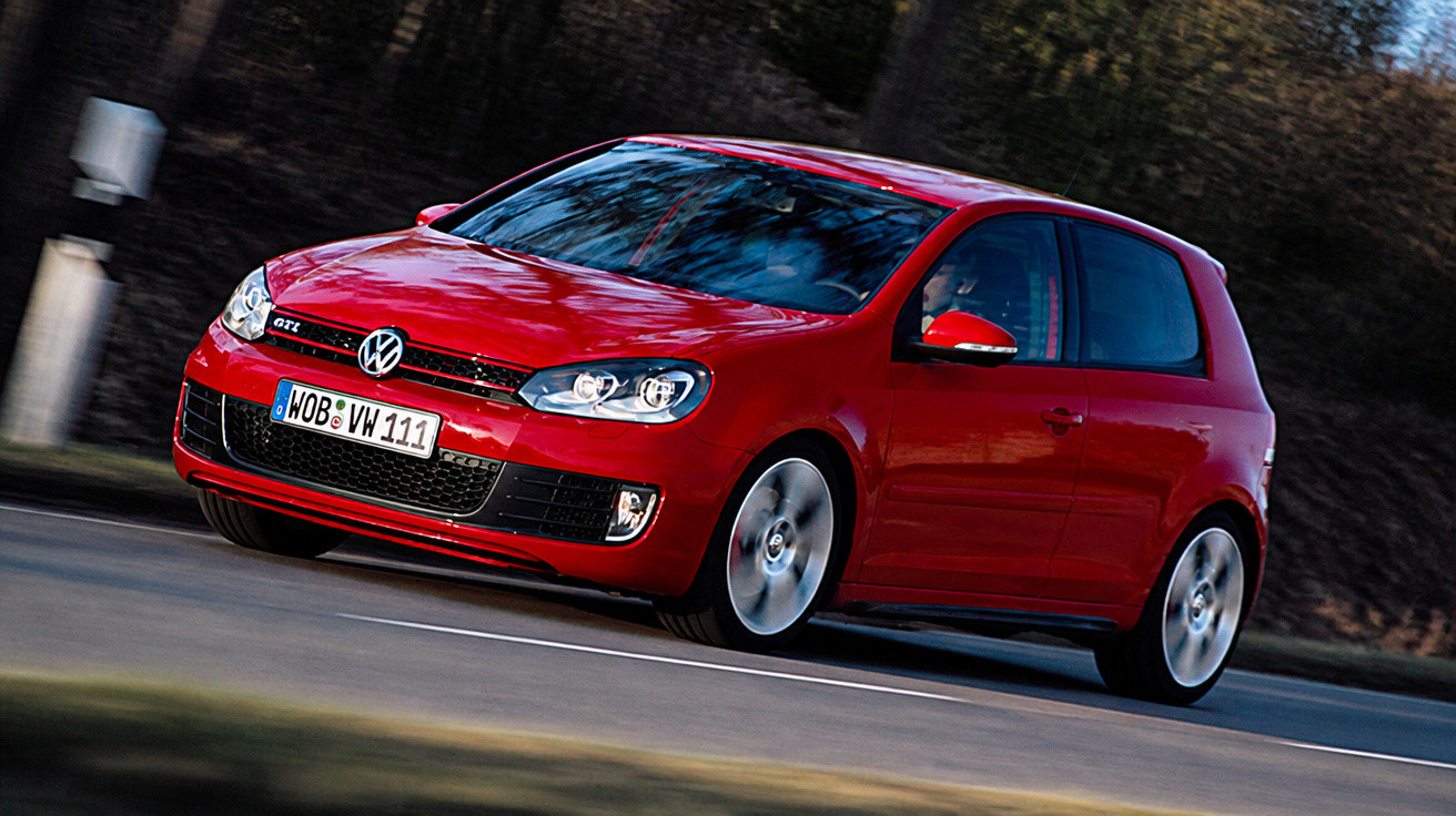 Red Volkswagen Golf GTI driving on a road with blurred background and motion effect.